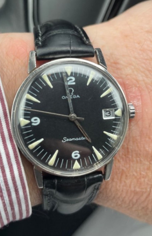 A near-identical Omega Seamaster with a black dial and date window, worn on the wrist on a black leather strap.